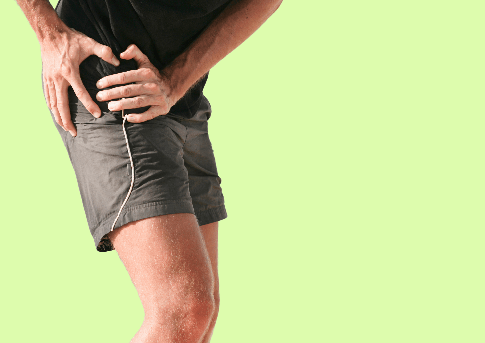 Mann in Shorts greift sich vor Schmerz mit beiden Händen an die Hüfte.