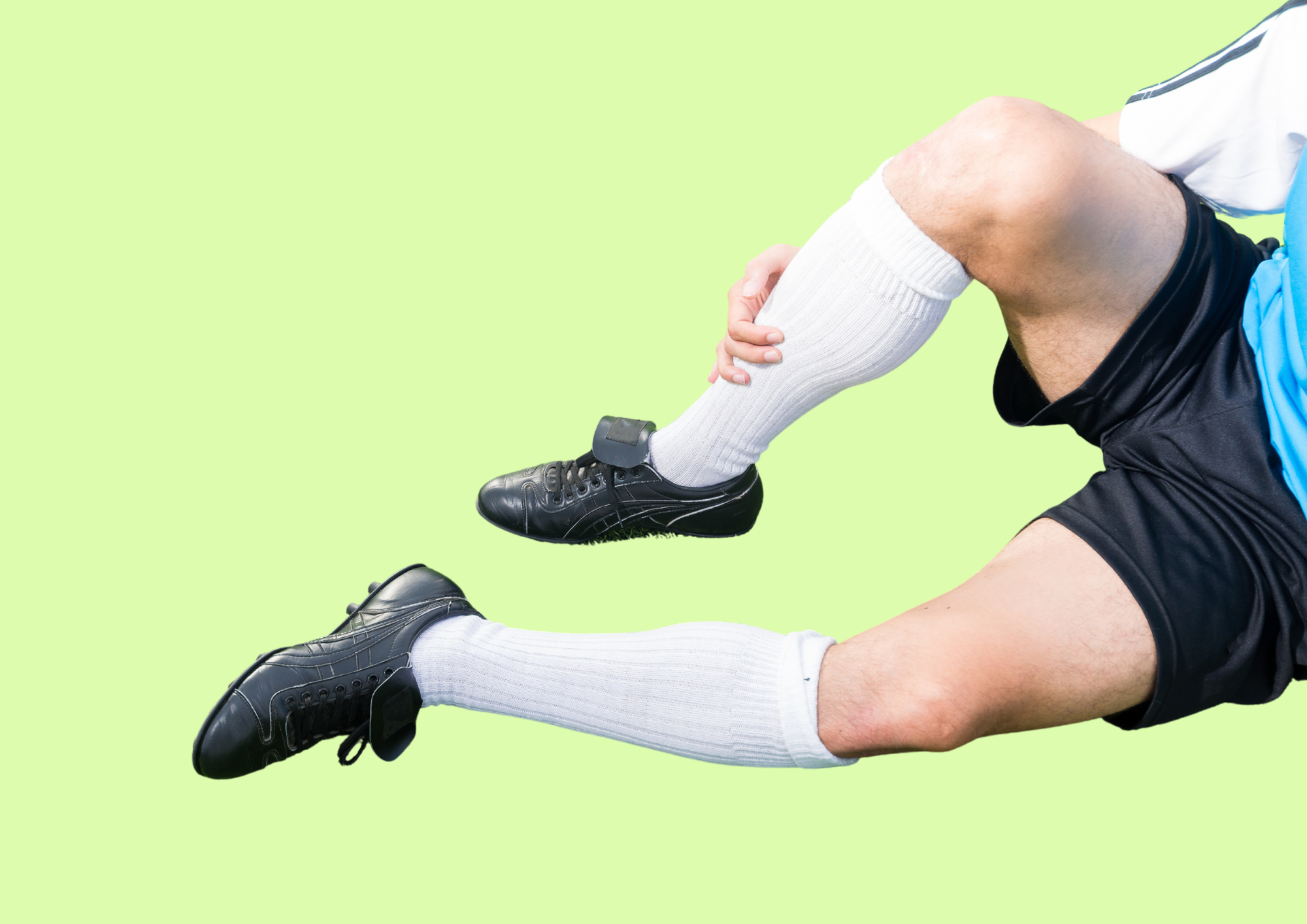 Fussballspieler sitzt auf dem Boden und fasst sich ans schmerzende Schienbein. Grüner Hintergrund.